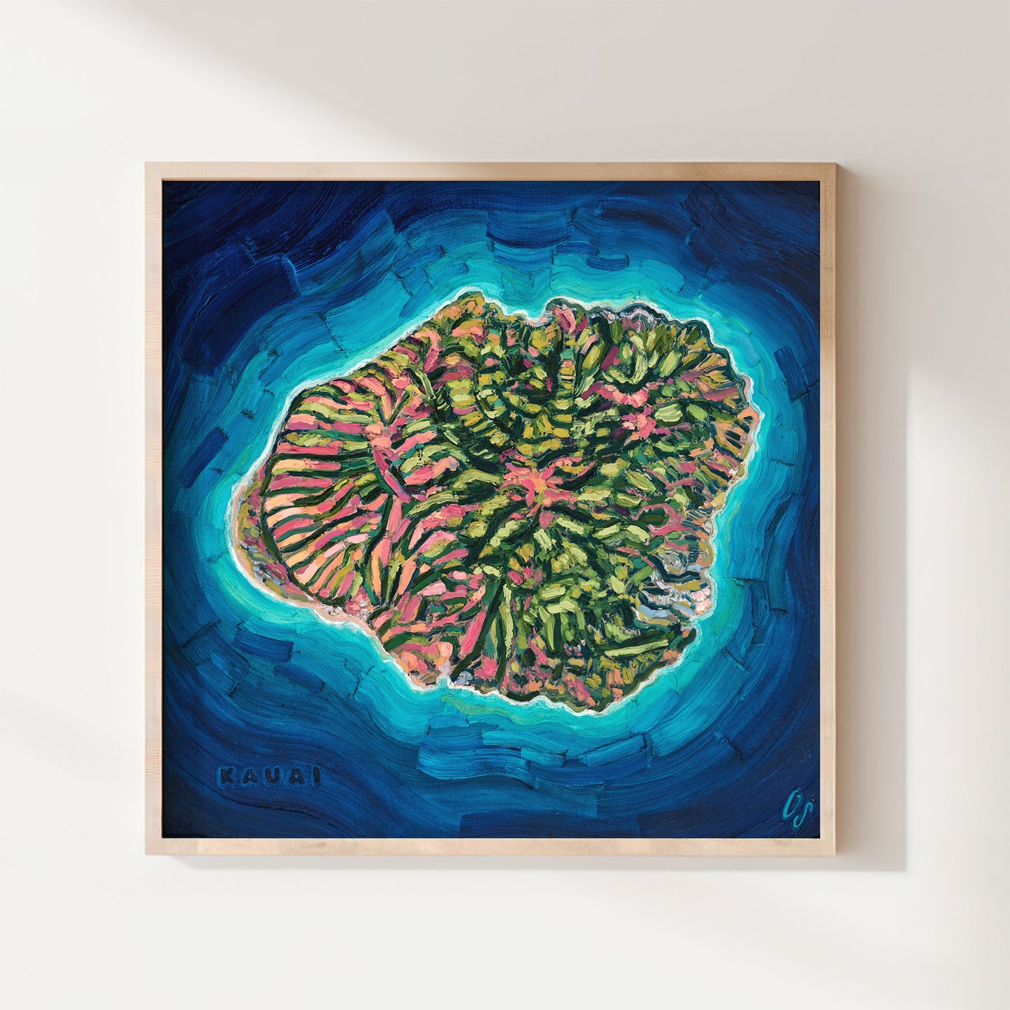 A framed square art print depicting a colorful coral reef island surrounded by deep blue and turquoise ocean water, hung on a light beige wall.